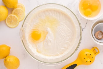 egg added to lemon meringue cheesecake batter in a glass bowl.