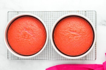 baked pink velvet cake layers in round cake pans on a wire rack.