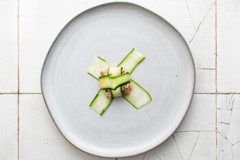 zucchini ribbons folded over a dollop of filling on a white plate.