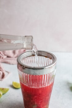 tequila poured over muddled strawberries in a cocktail shaker.