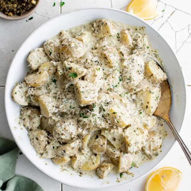 overhead view of pesto potato salad in a white bowl with a spoon.