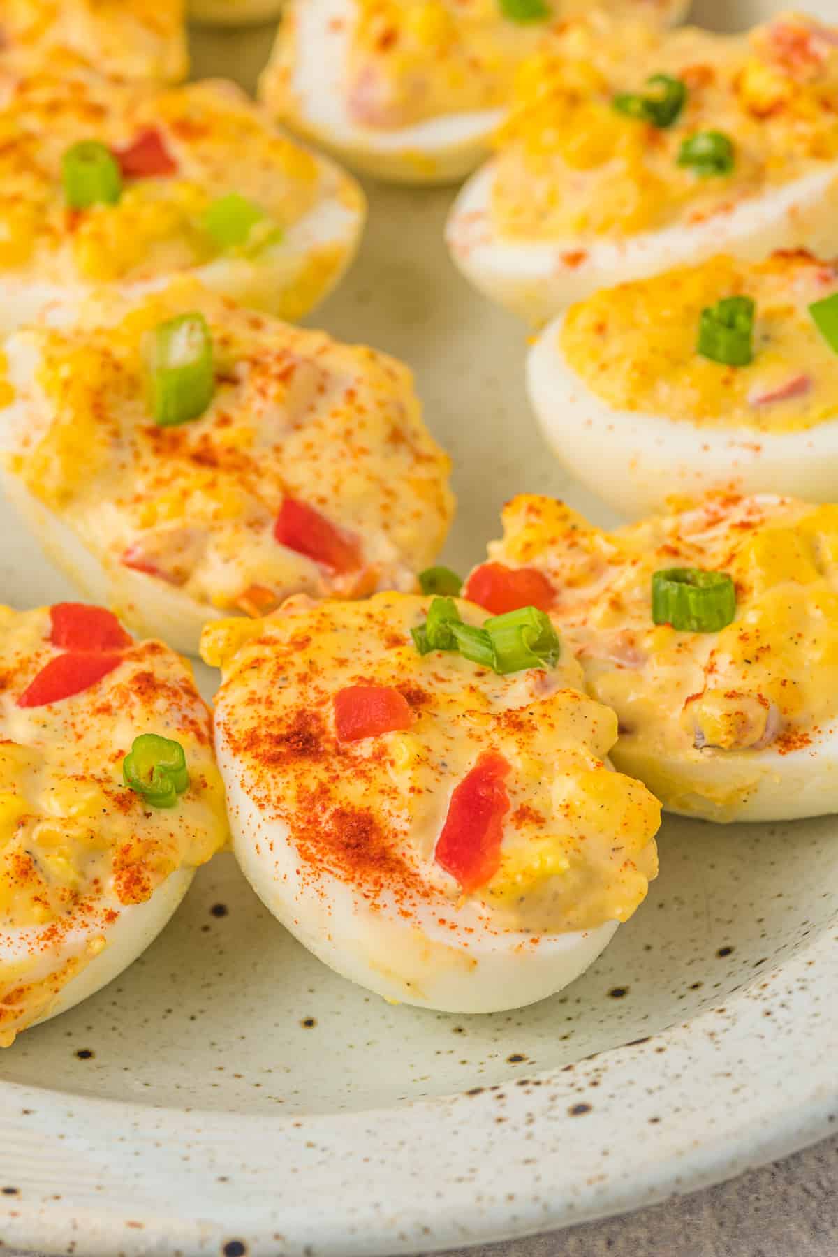 close up of deviled eggs with pimento cheese on a white oval serving tray.