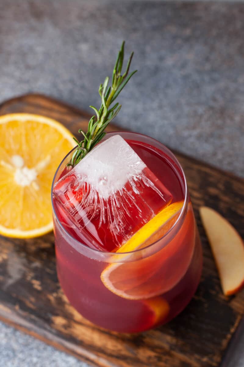 close up three-quarters view of red sangria in a stemless wine glass with ice and rosemary.