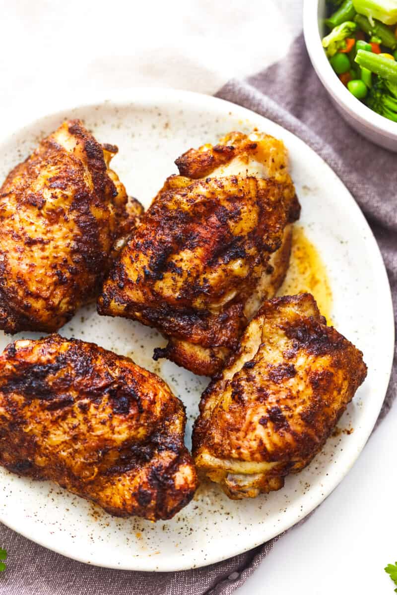 overhead view of 4 air fryer chicken thighs on a white plate.