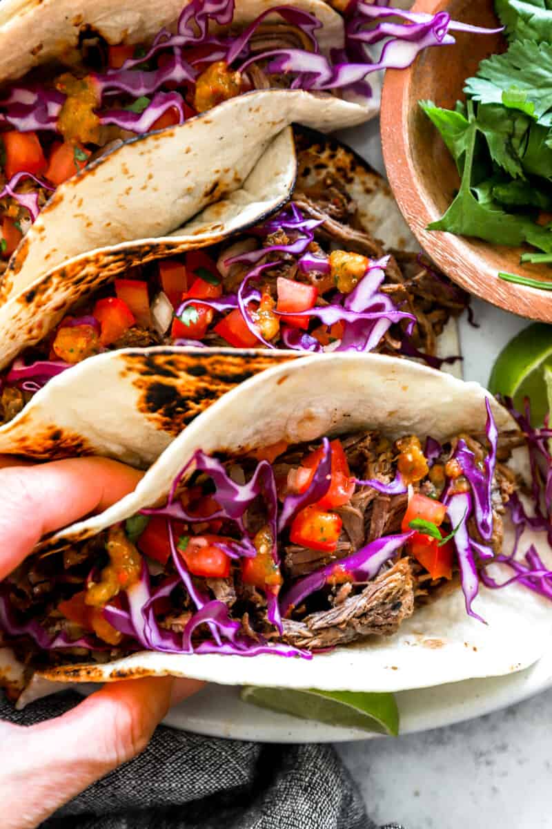 a hand grabbing a barbacoa taco from a marble tabletop.