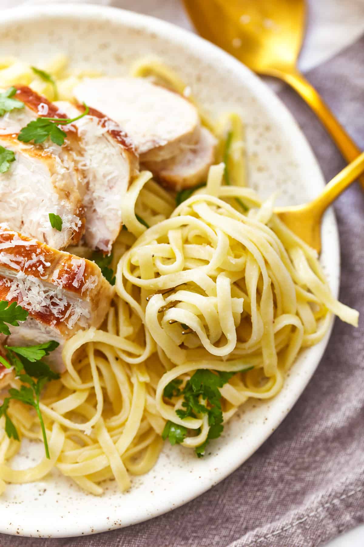 a forkful of chicken alfredo hovering above a serving of chicken alfredo on a white plate.