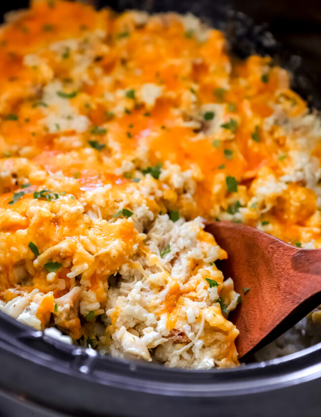 a wooden spoon lifting crockpot chicken and rice from a crockpot.