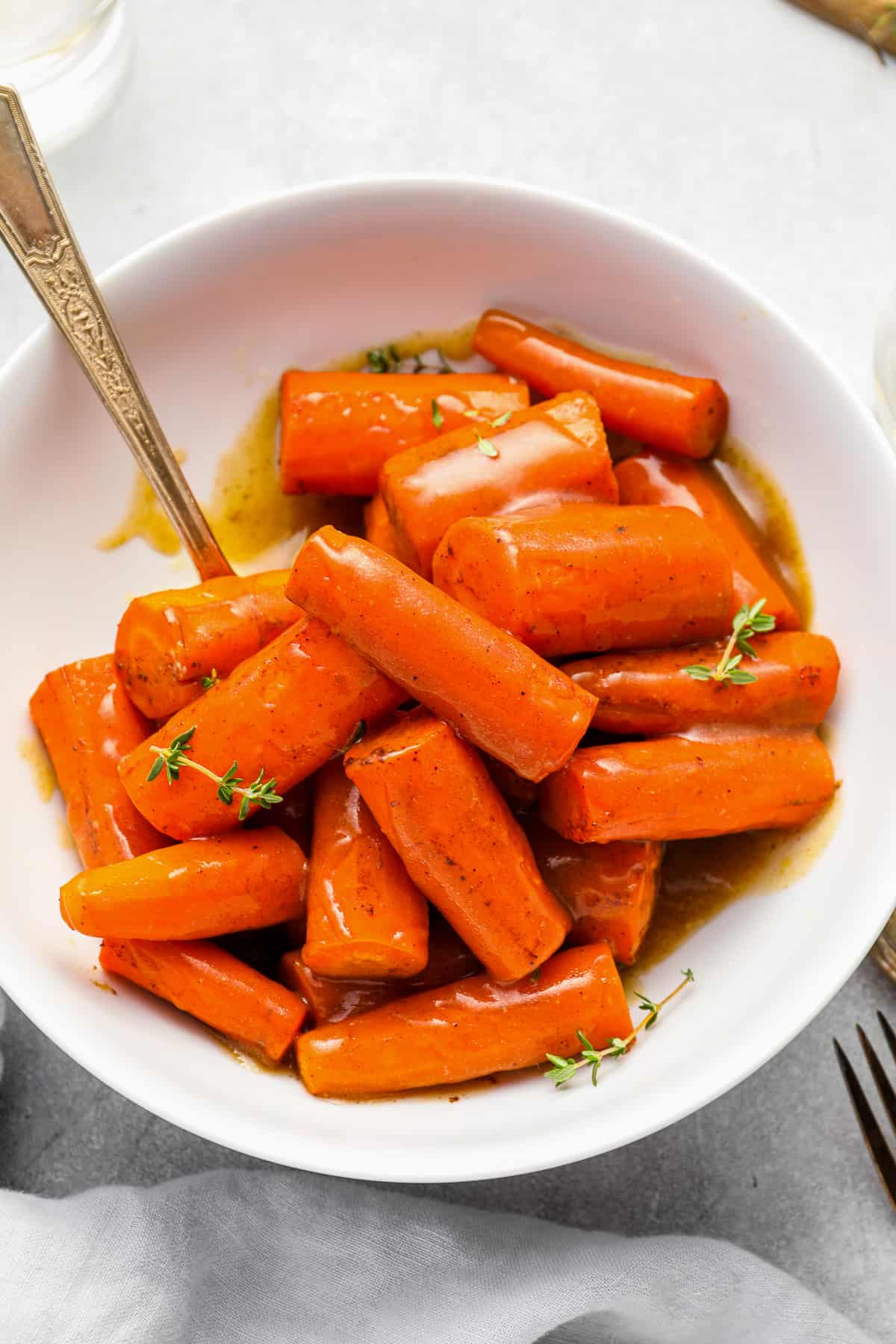 crockpot carrots in a white bowl with a serving spoon.