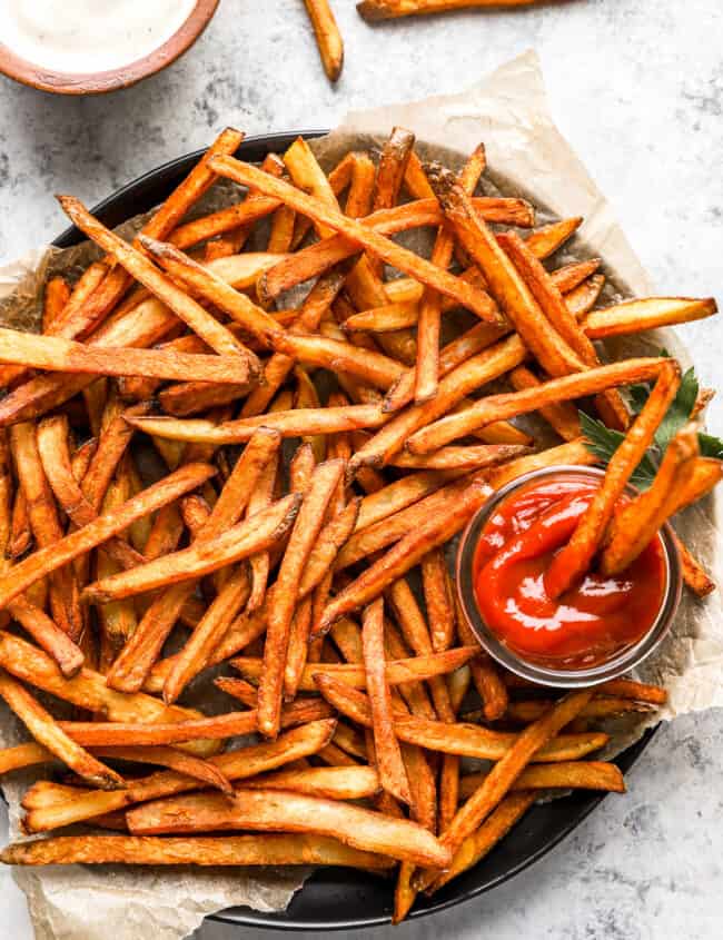 homemade french fries on a round serving tray with a cup of ketchup.