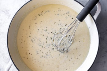 homemade alfredo sauce in a white dutch oven with a whisk.