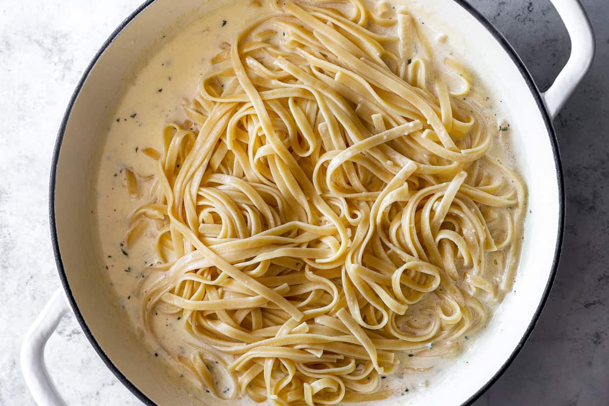 pasta added to homemade alfredo sauce in a white dutch oven.