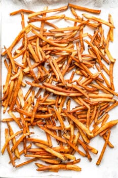 homemade french fries spread out on a paper towel-lined baking sheet.