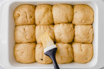 proofed hot cross bun dough balls in a rectangular baking pan brushed with egg wash.