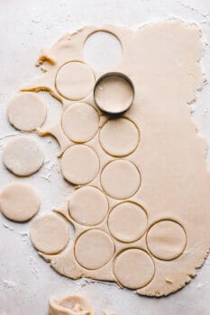 a circular cookie cutter cutting cookies out of a sheet of cookie dough.