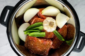 onion chunks, serrano peppers, and a head of garlic on top of seasoned pork shoulder chunks in an instant pot.