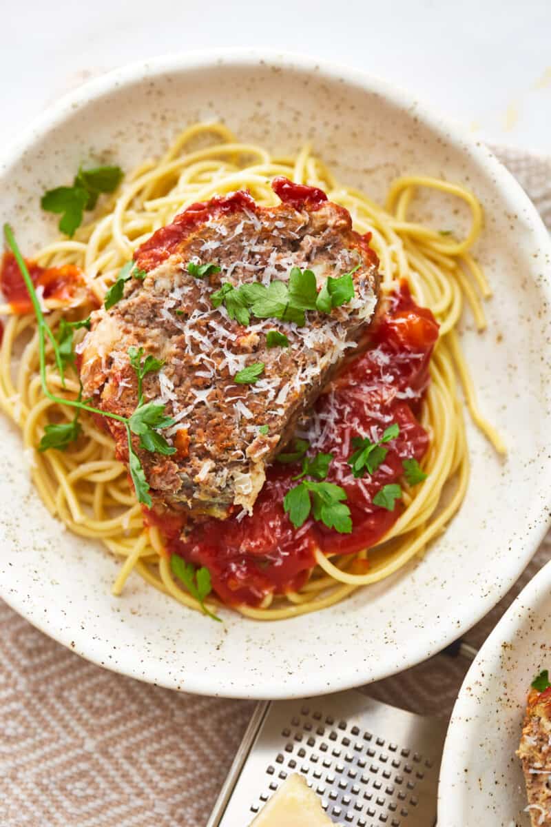 overhead view of a slice of mozzarella stuffed meatloaf on a bed of pasta in a white bowl.