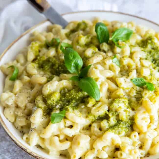 three-quarters view of a bowl of pesto mac and cheese with a fork.