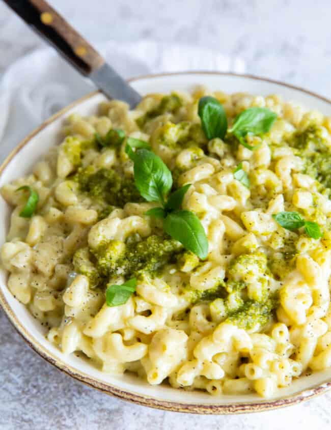 three-quarters view of a bowl of pesto mac and cheese with a fork.