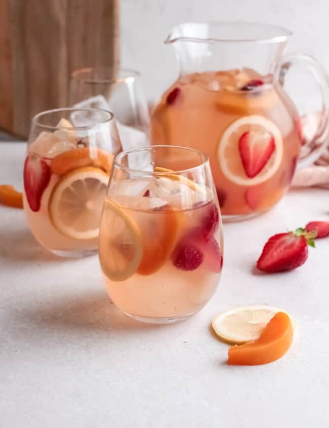 three-quarters view of 2 glasses of rose sangria in front of a pitcher.