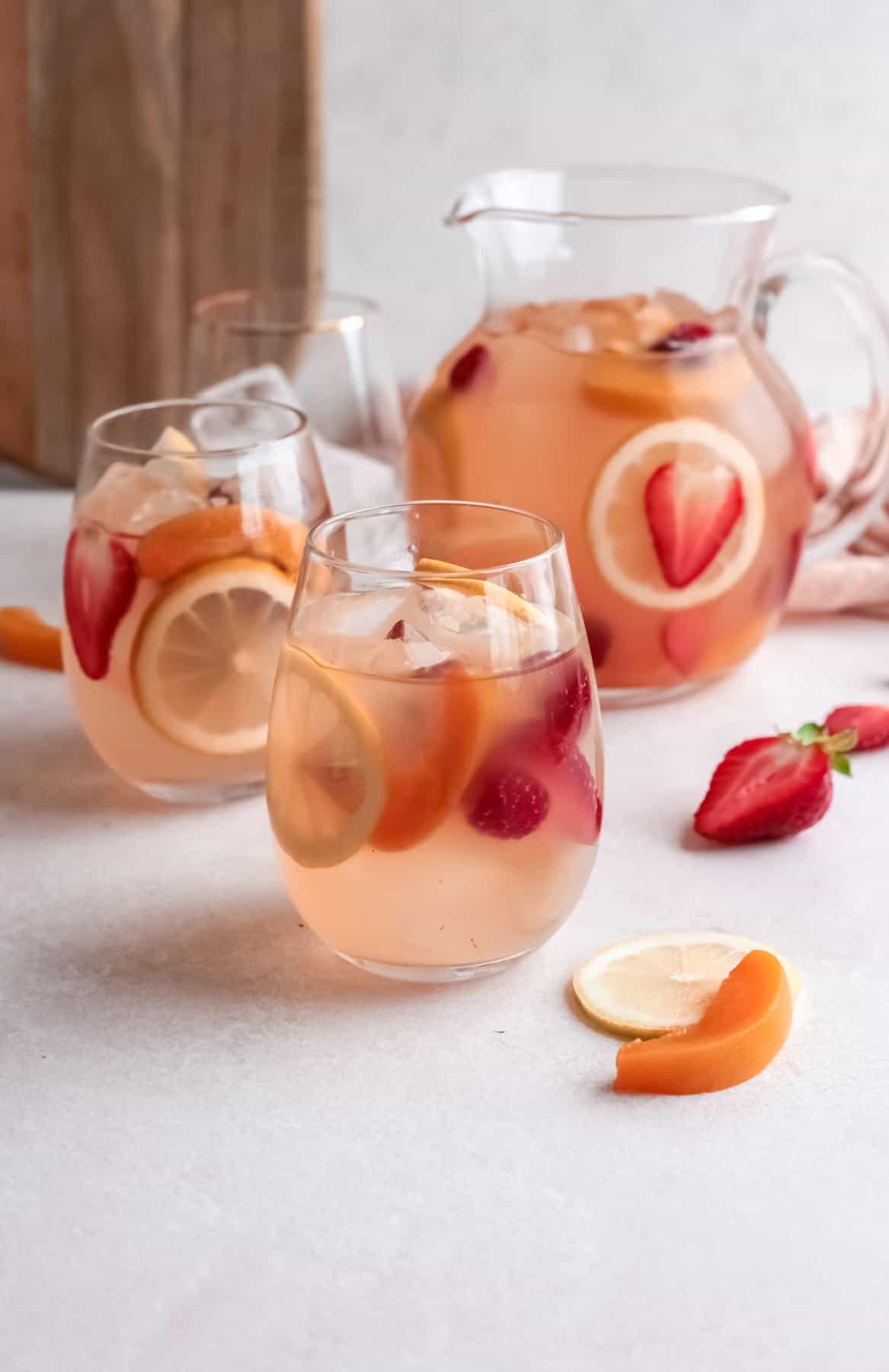 three-quarters view of 2 glasses of rose sangria in front of a pitcher.