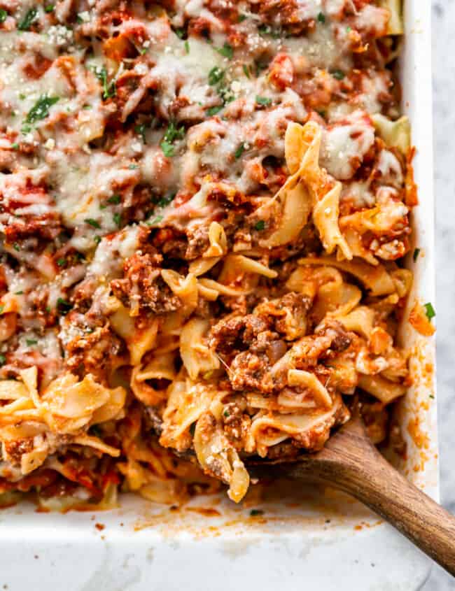 three-quarters view of the lower right corner of a sour cream noodle casserole with a wooden spoon.