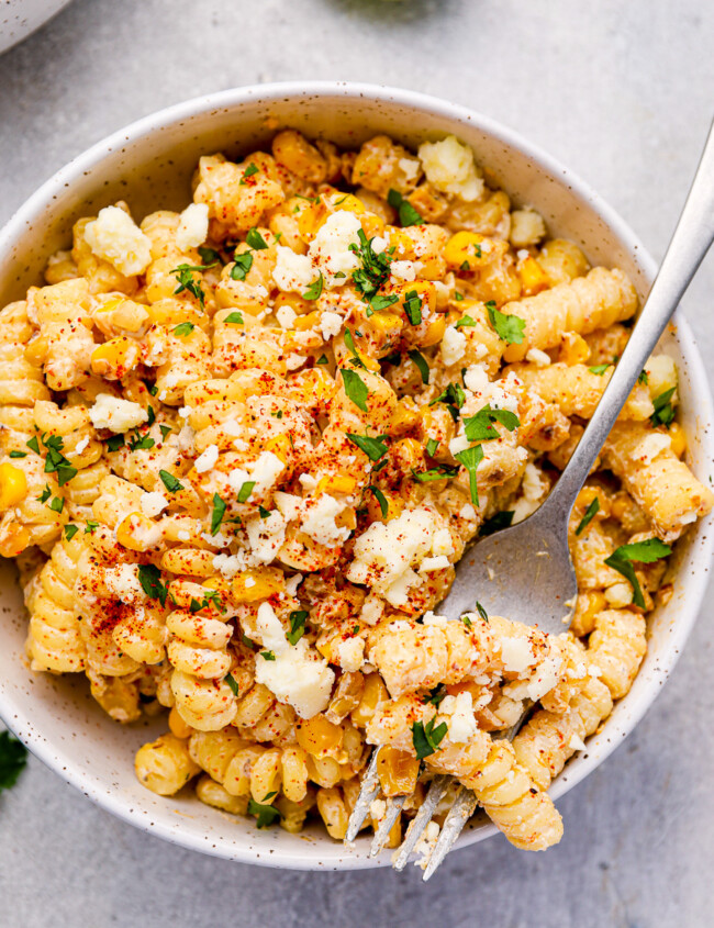 overhead view of a serving of street corn pasta salad in a white bowl with a fork.