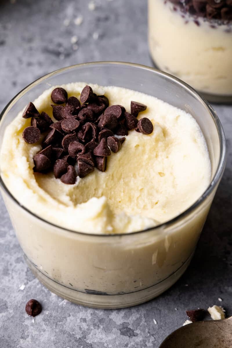 three-quarters view of white chocolate mousse in a small glass cup with a bite missing topped with chocolate chips.