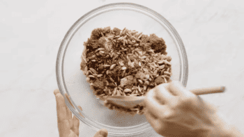 A person blending brown sugar and nuts in a glass bowl.