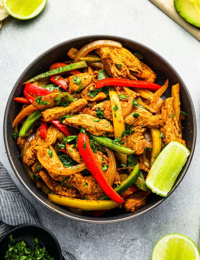 overhead view of chicken fajita filling in a black bowl with a lime wedge.