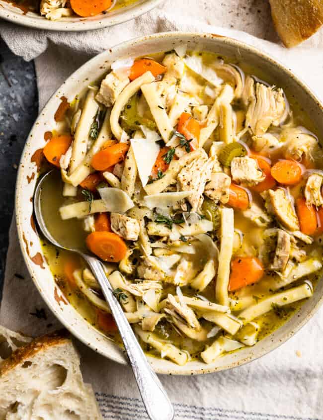 overhead view of a serving of chicken noodle soup in a white bowl with a spoon.