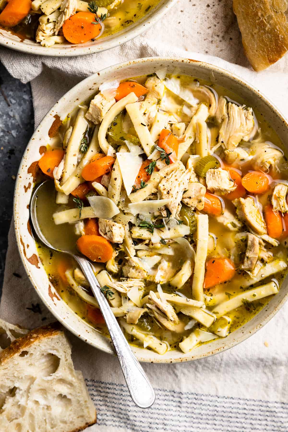 overhead view of a serving of chicken noodle soup in a white bowl with a spoon.