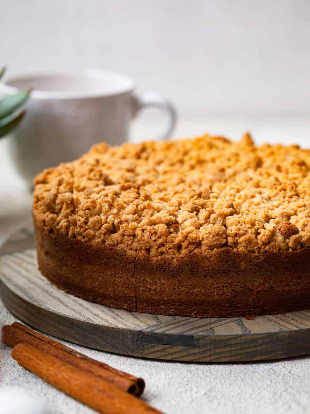 side view of a cake mix coffee cake on a cake plate with cinnamon sticks in front of it.