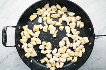 partially cooked cubed chicken in a frying pan.