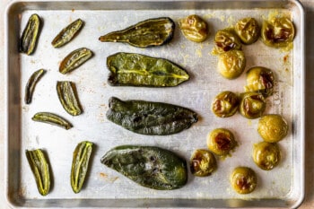 roasted tomatillos and halved peppers on a baking sheet.