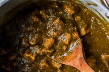 close up view of chile verde in a dutch oven with a wooden spoon.