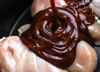 bbq sauce being poured over chicken in a pan.