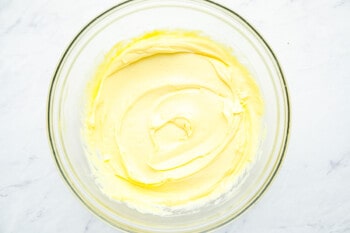 oil added to whipped egg yolks, mustard, and vinegar in a glass bowl.