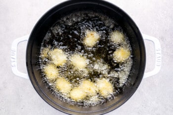 tater tots frying in a white and black dutch oven.