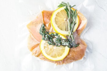 2 raw chicken breasts in a vacuum sealed bag with lemon slices and herbs.