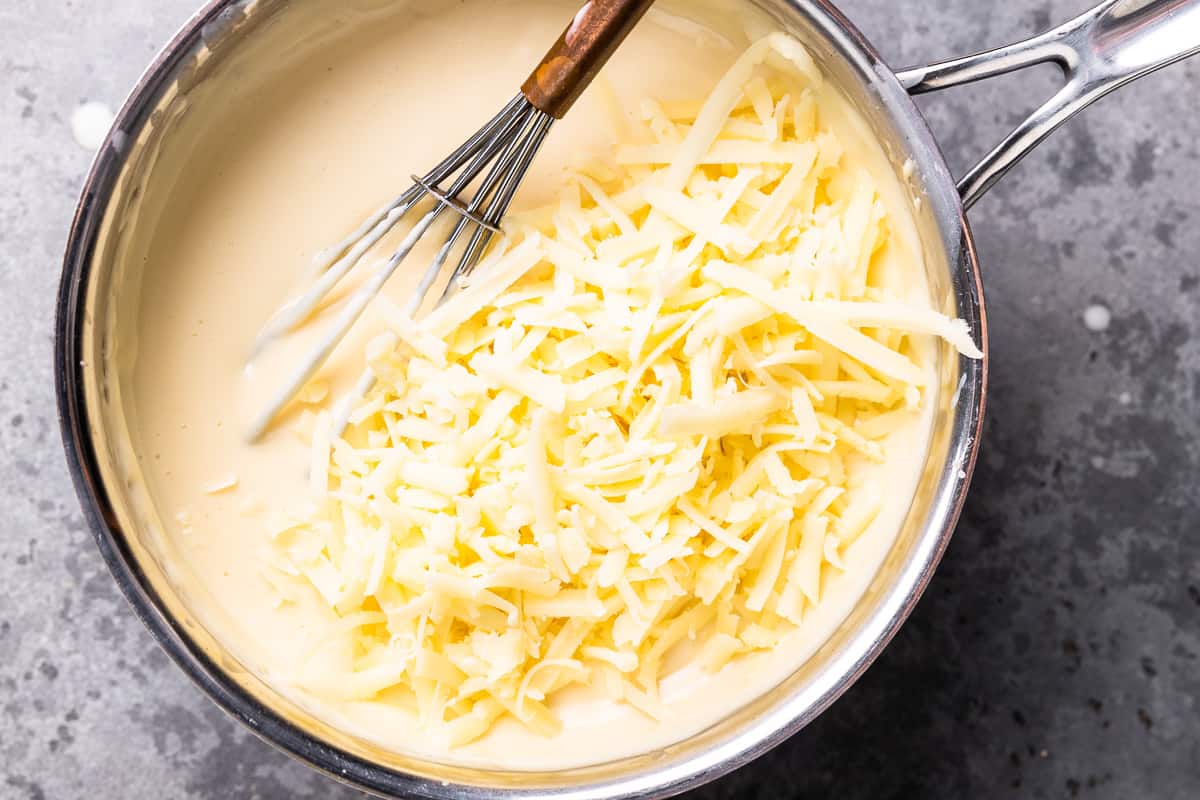 shredded cheese added to white queso in a saucepan with a whisk.