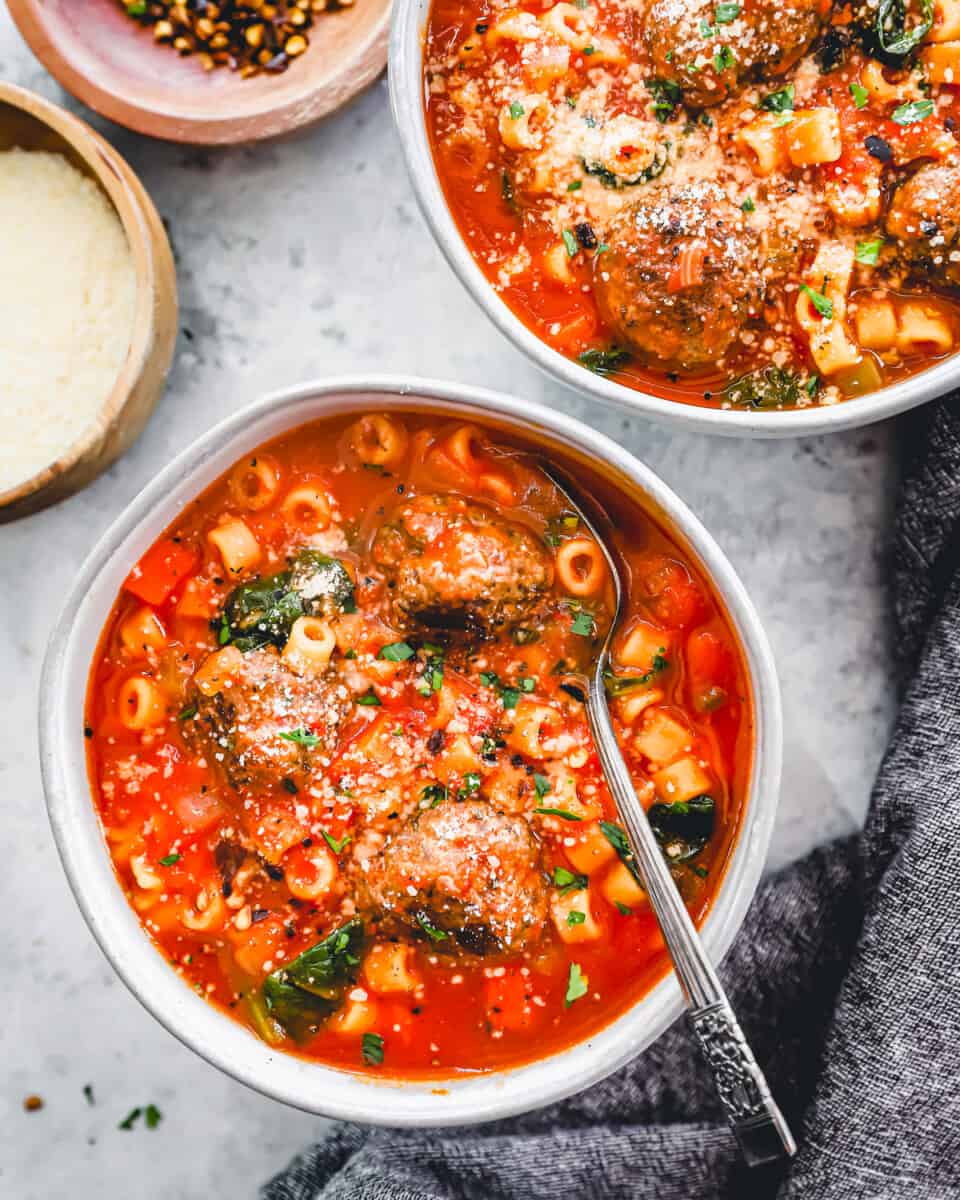 overhead view of 2 servings of meatball soup with pasta in white bowls, one has a spoon.