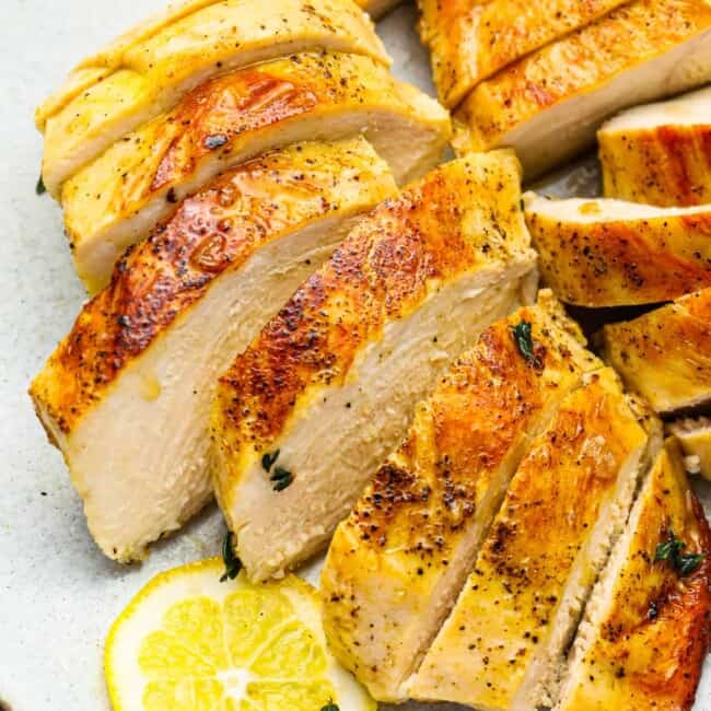 three-quarters view of 2 sliced sous vide chicken breasts on a white plate with a lemon slice.