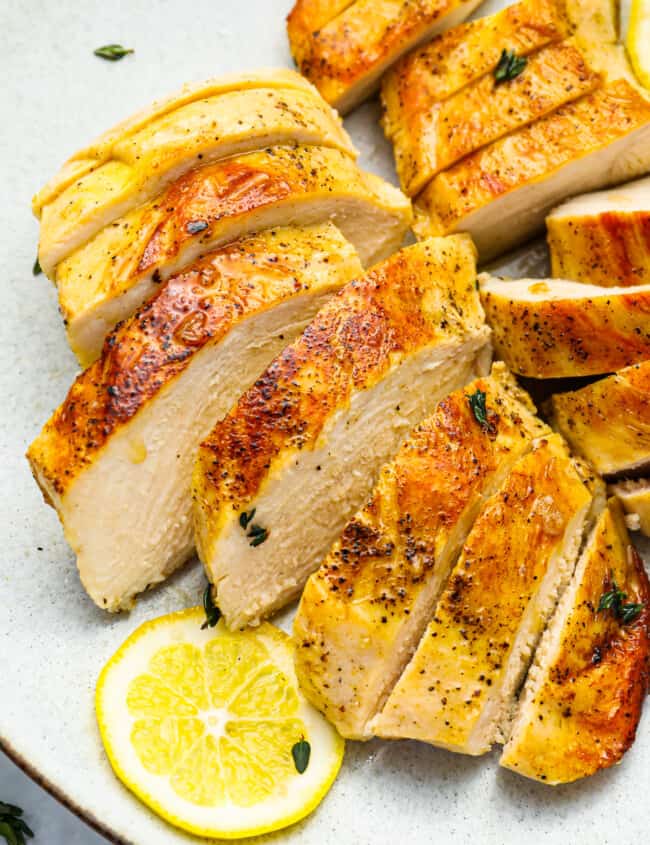 three-quarters view of 2 sliced sous vide chicken breasts on a white plate with a lemon slice.