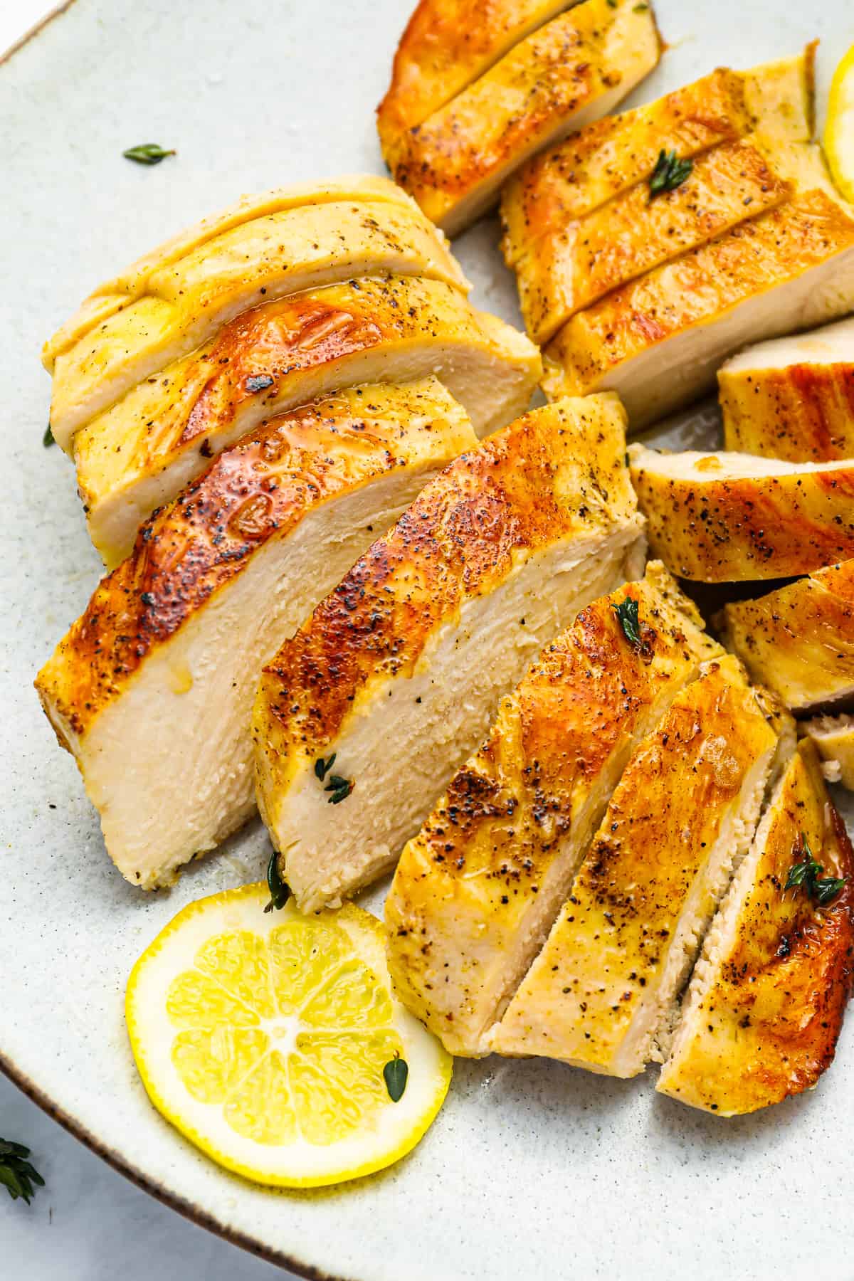 three-quarters view of 2 sliced sous vide chicken breasts on a white plate with a lemon slice.