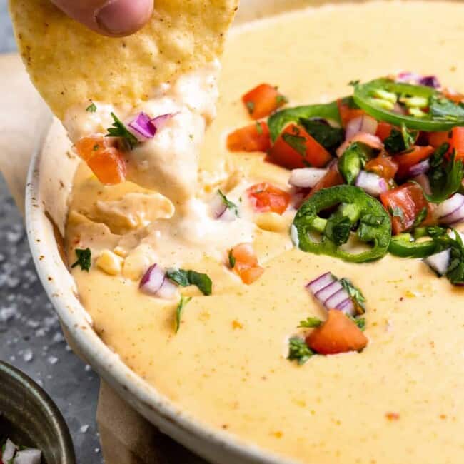 a person dipping a tortilla into a bowl of mexican dip.