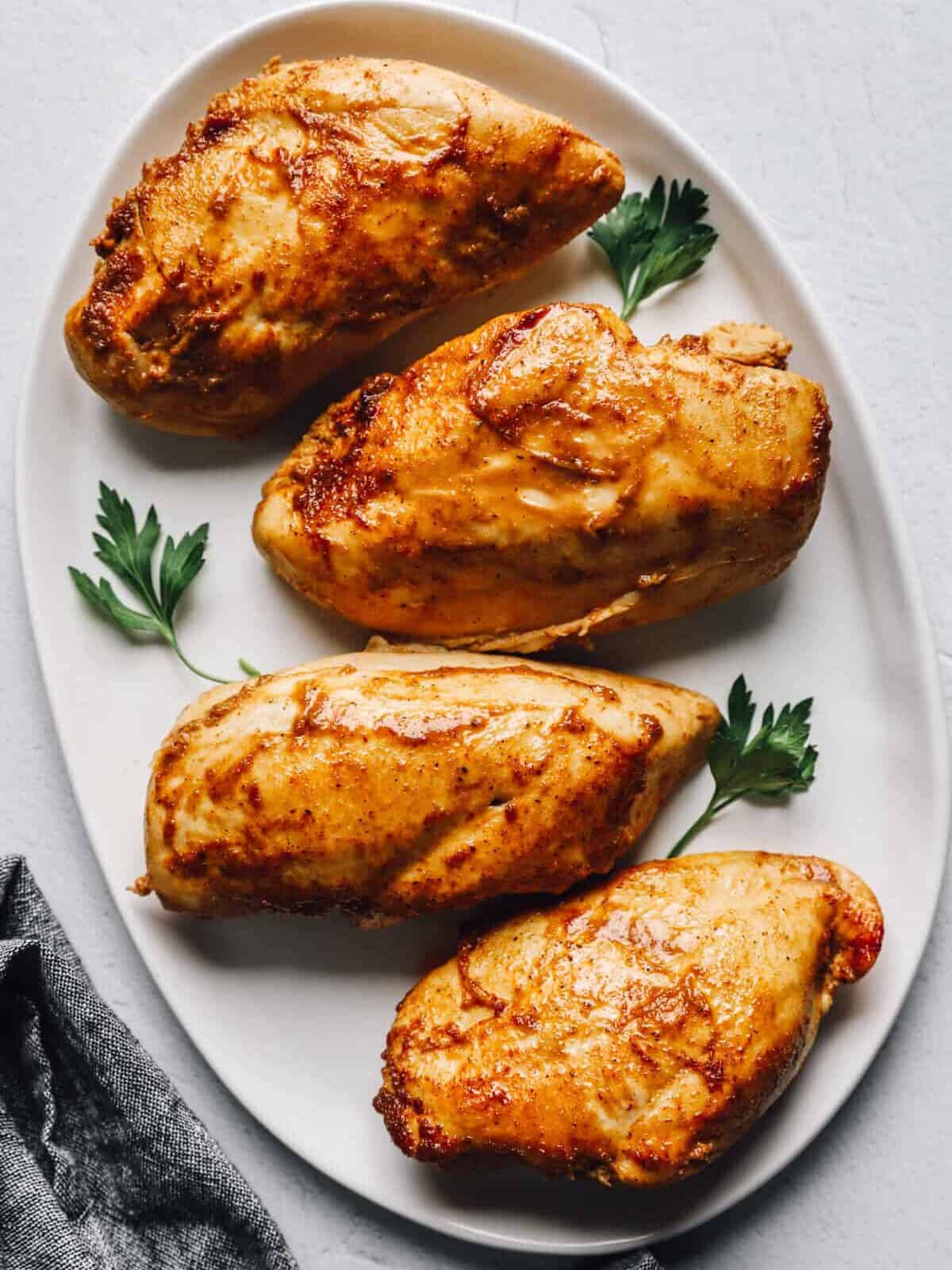 overhead view of marinated baked chicken breasts on a white oval serving platter.