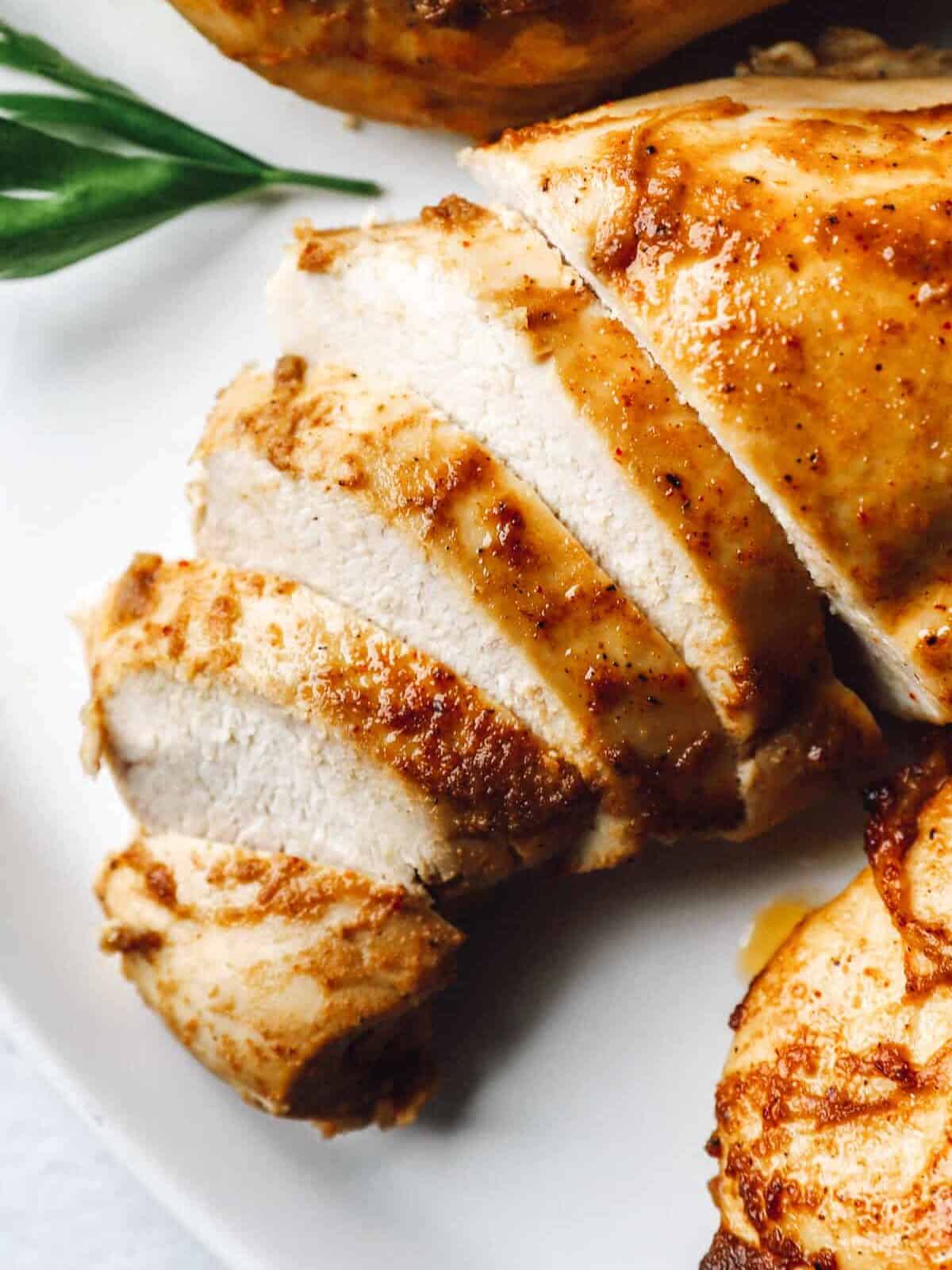 close up of a partially sliced baked marinated chicken breast on a white platter.