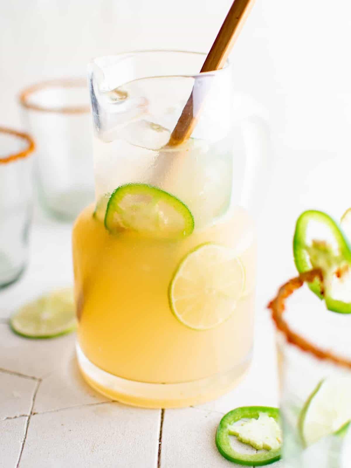 a pitcher of spicy jalapeño margaritas surrounded by glasses