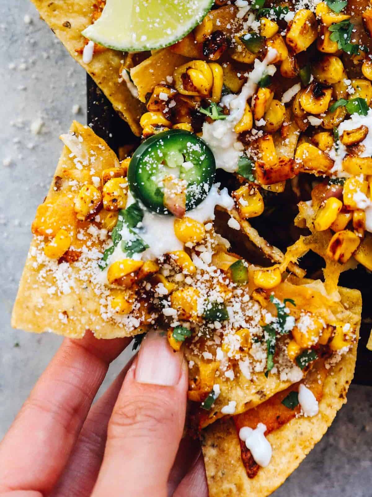 close up of a hand grabbing street corn nachos from a baking sheet.