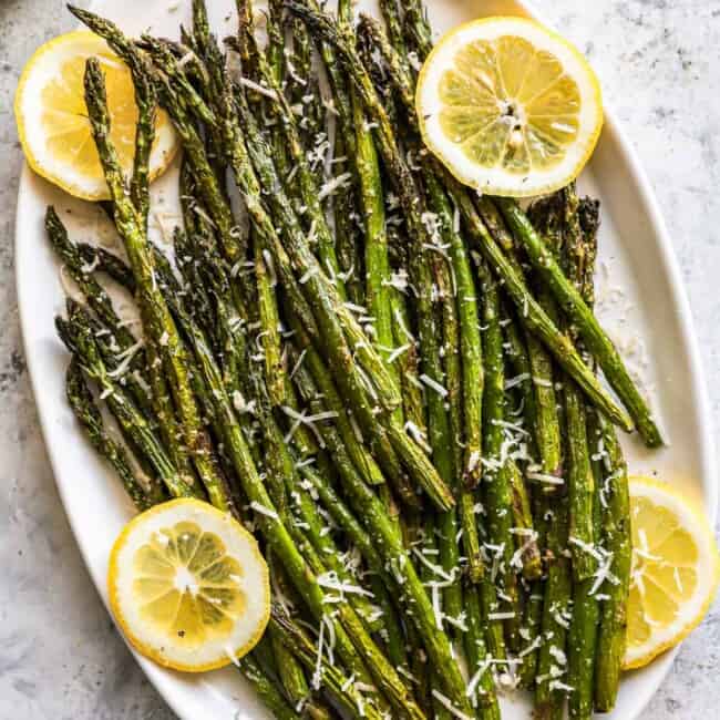 overhead view of air fryer asparagus on a white oval serving platter with lemon slices.